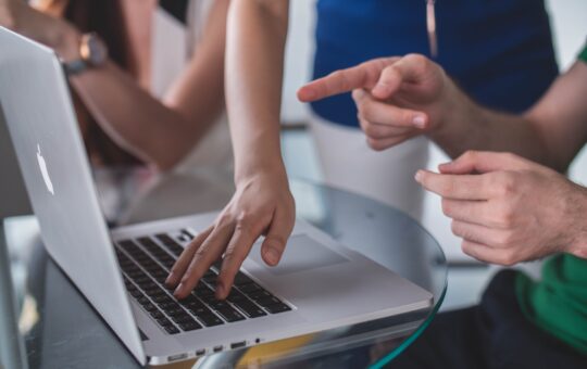 A group of people sitting around a laptop.