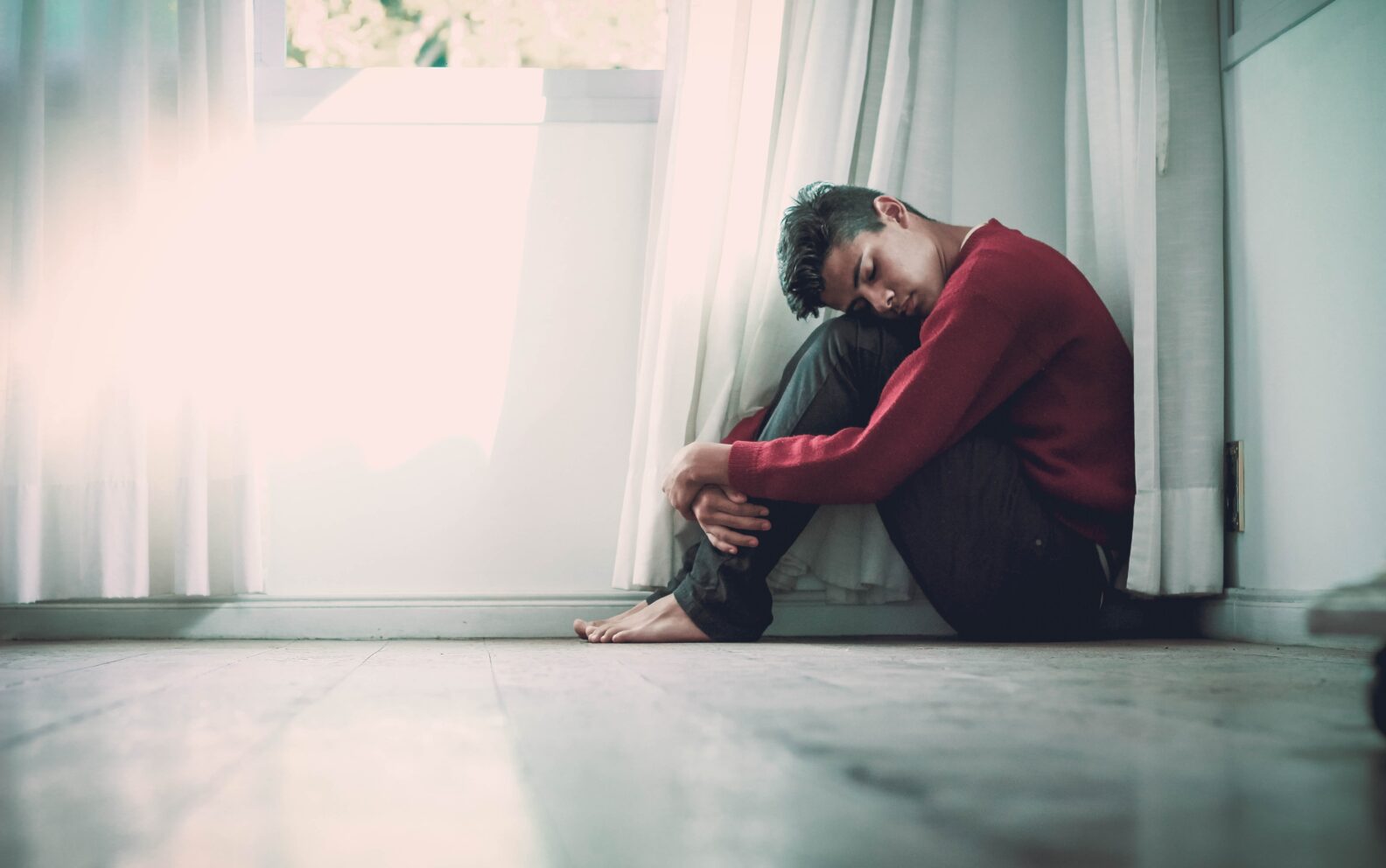 A person sitting on the ground in front of a window.